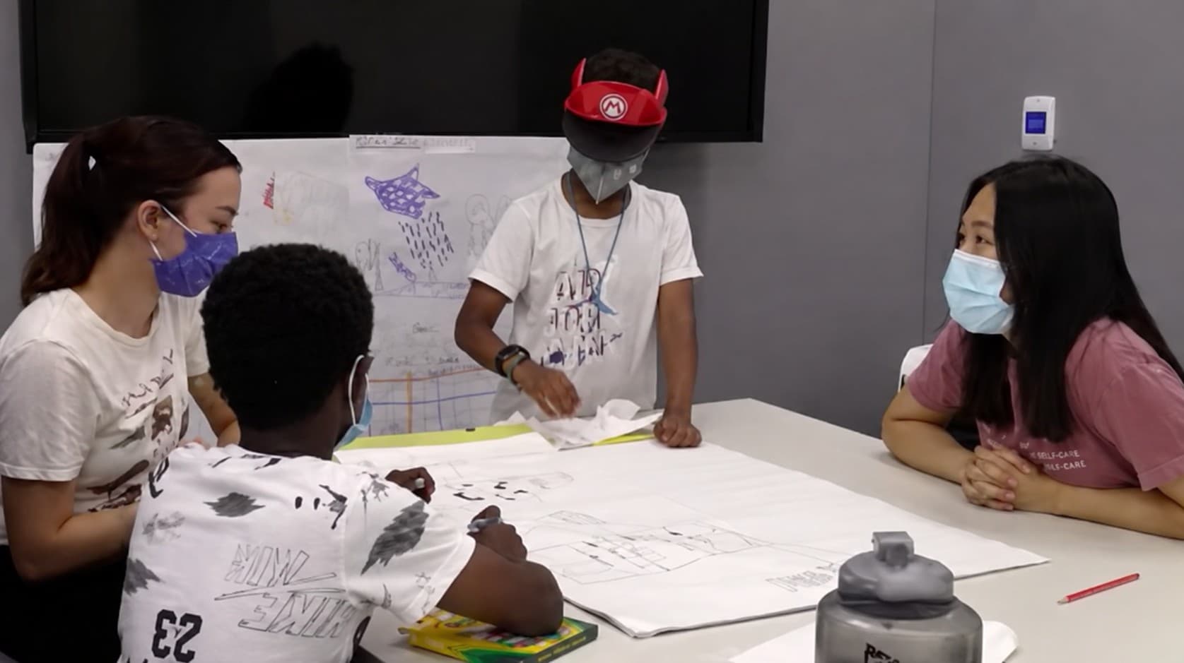 Children and adult researchers co-designing around a table covered in large sheets of paper